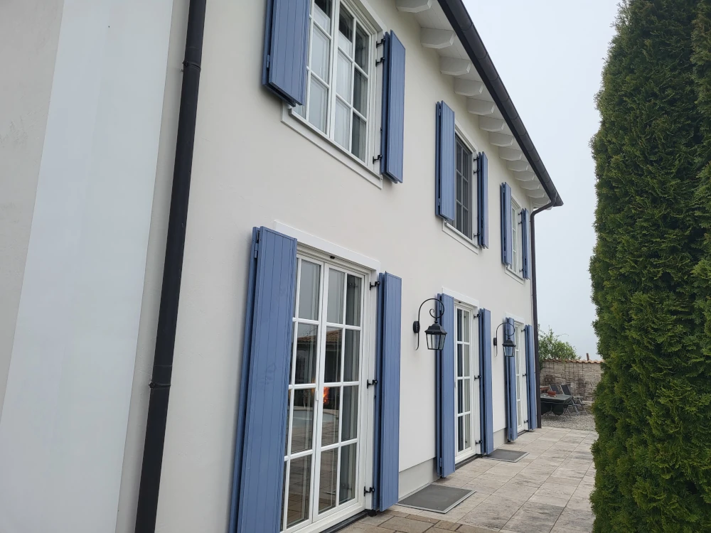 Weiße Dachuntersicht und sanierte Fassade mit blauen Fensterläden