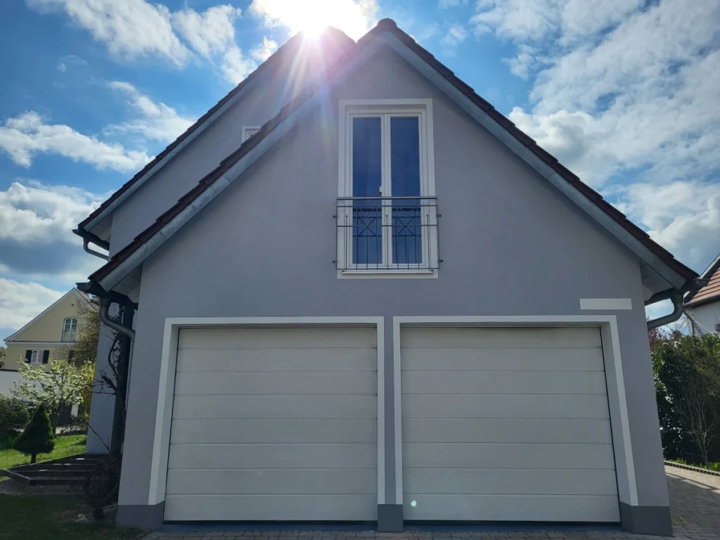 Hellgraue Giebelfassade mit weißen Garagentoren und farblich abgesetztem Sockel