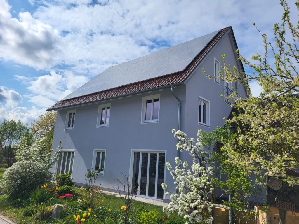 Frisch gestrichene hellgraue Hausfassade mit weißer Dachuntersicht und blühendem Garten